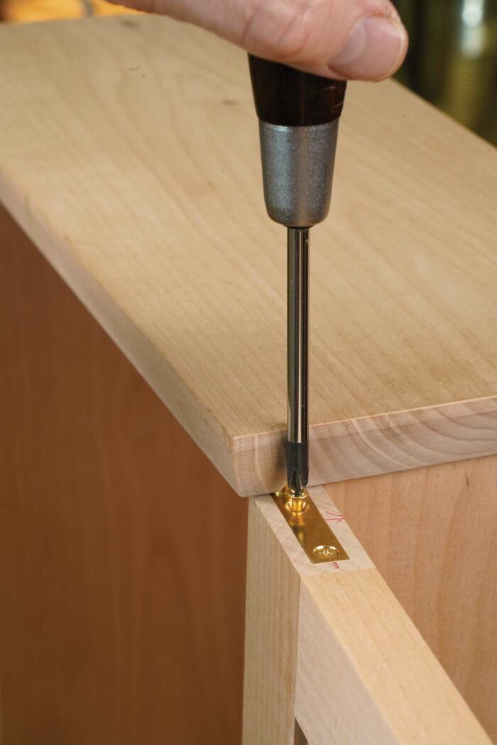 Install the hinge leaf in the bottom of the door, and then drop the door onto the pivot pin of the lower case hinge. Now hold the upper door leaf in place on the case leaf’s pivot as you tilt the door and slide the leaf into its mortise. Then drive the last two screws.